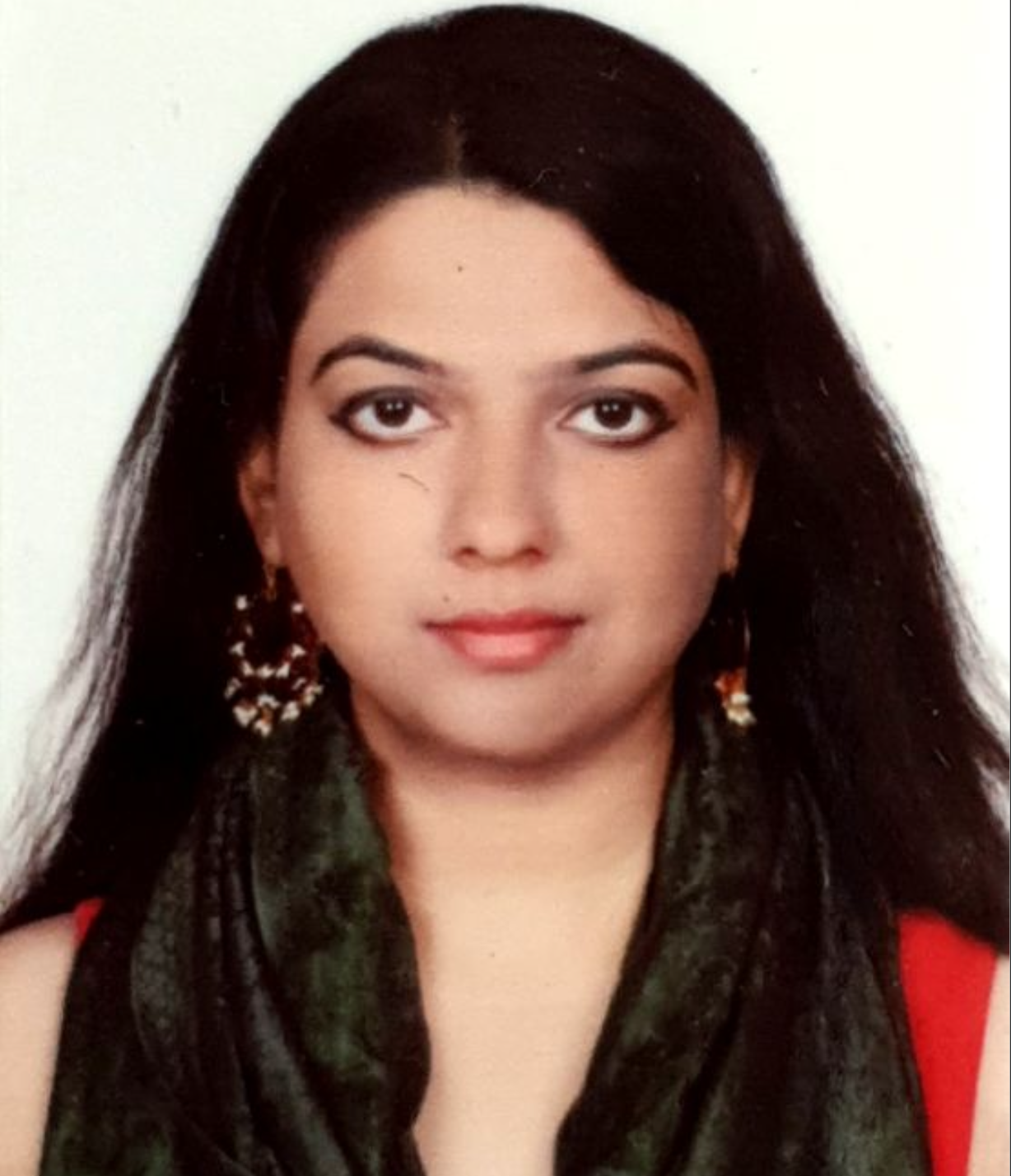 
Smiling South Asian cis-woman with long black hair wearing a red top, green shawl and large earrrings.